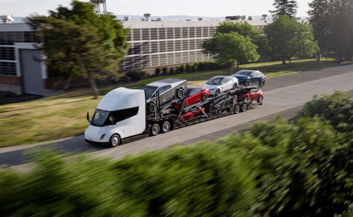 Futuristic electric semi-truck hauling multiple vehicles on a highway.