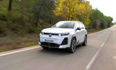 A white electric SUV driving on a forest road in autumn.