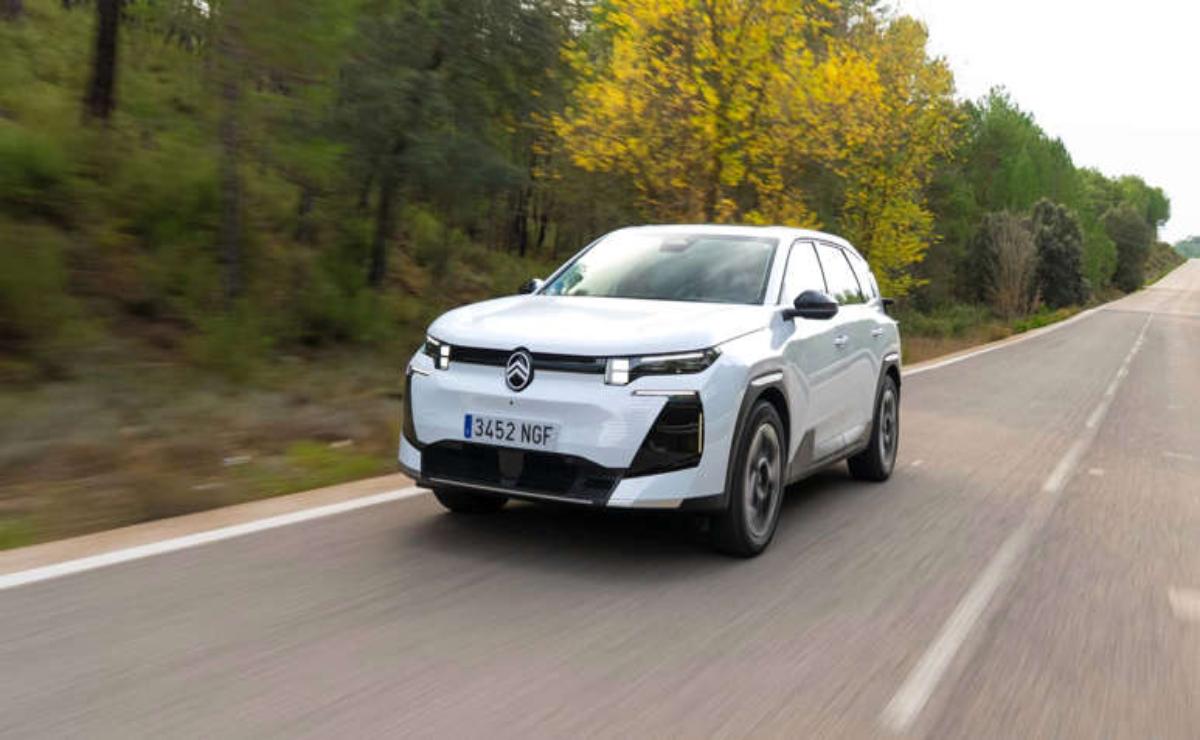 A white electric SUV driving on a forest road in autumn.