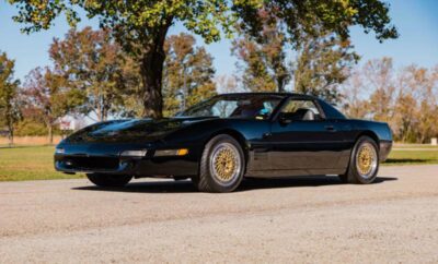 A classic black sports car parked on a sunny dirt road.