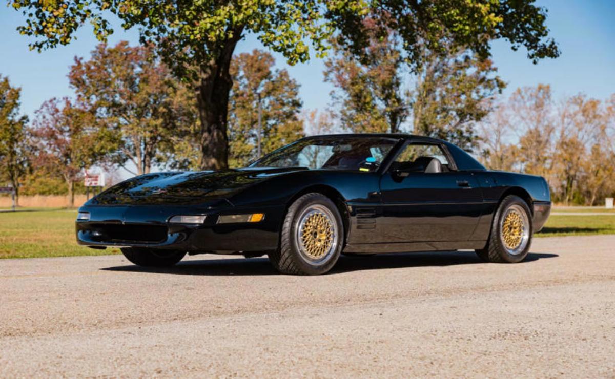 A classic black sports car parked on a sunny dirt road.