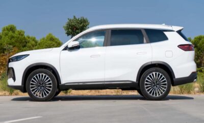 White modern SUV parked on a road with trees in the background.