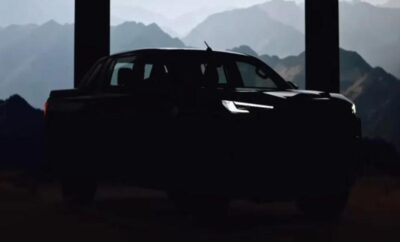 Silhouetted car with glowing headlights against a mountainous backdrop.