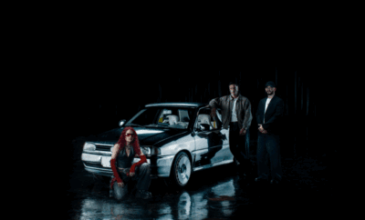 Three individuals posing with a classic police car in a dark setting.