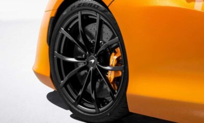 Close-up of a sleek black car wheel with orange brake calipers on an orange sports car.