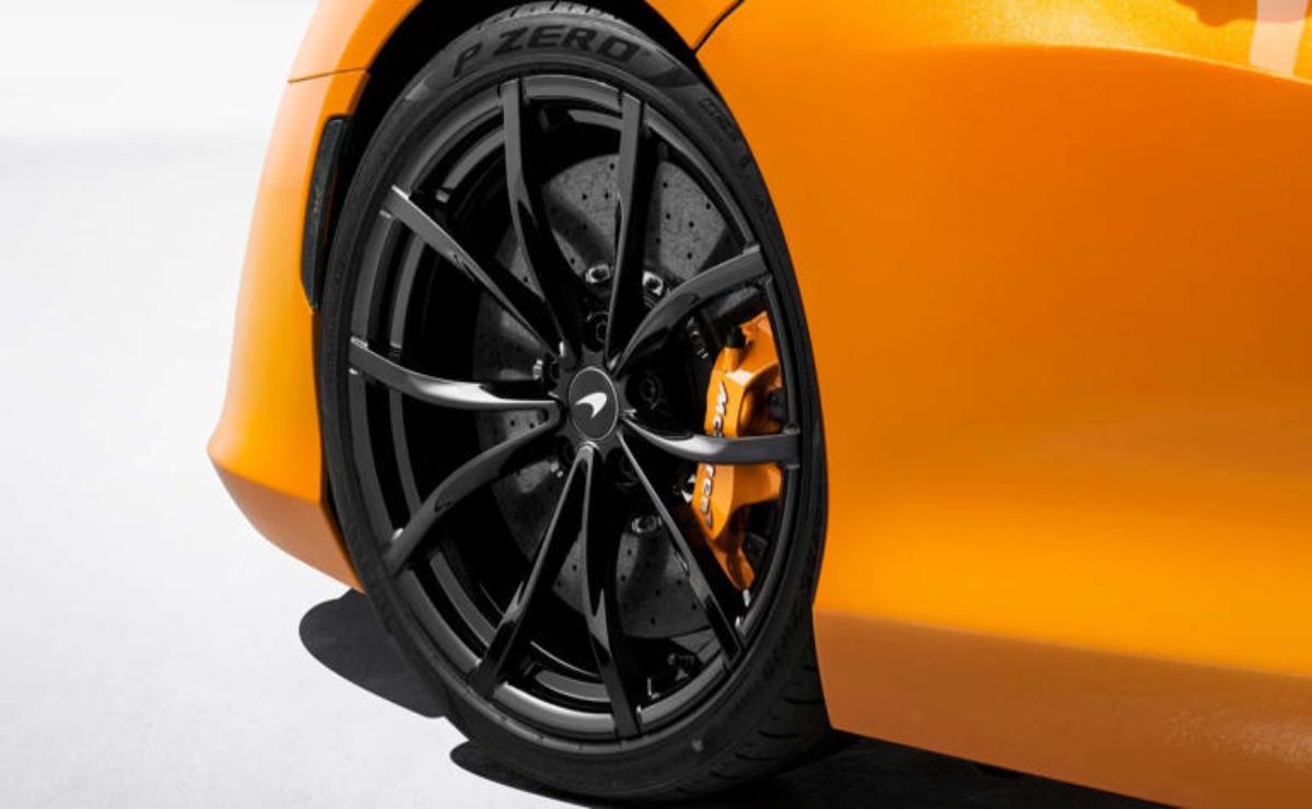 Close-up of a sleek black car wheel with orange brake calipers on an orange sports car.