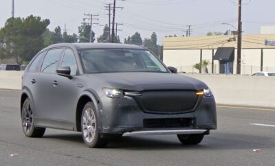 A sleek gray car drives on a street with power lines in the background.