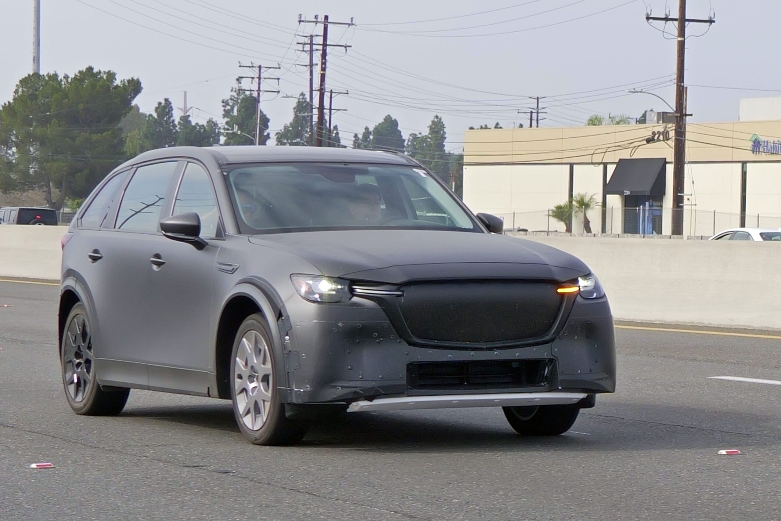 A sleek gray car drives on a street with power lines in the background.