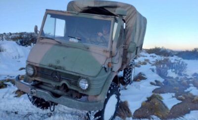 Military truck with snow chains on tires in a snowy terrain.