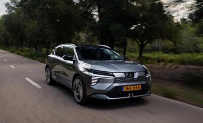 A sleek grey electric SUV driving on a road surrounded by trees.