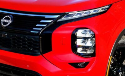 Close-up of a red vehicle's modern headlight and grille design.