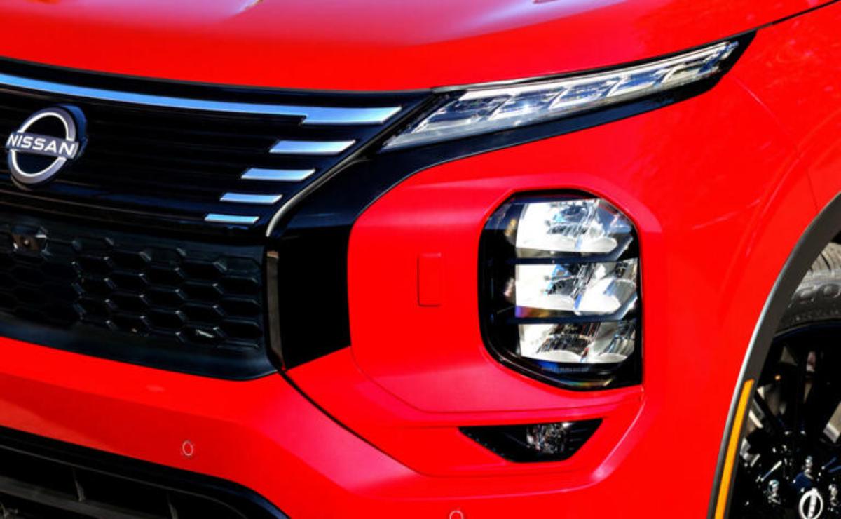 Close-up of a red vehicle's modern headlight and grille design.