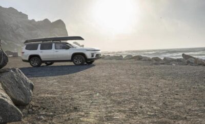 White camper van parked near the beach with mountains in the background.