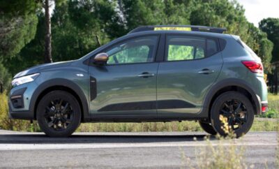 Side view of a green SUV parked on a road with trees in the background.