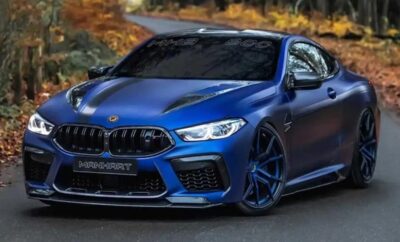 Sleek blue BMW M8 sports car on a road surrounded by autumn foliage.