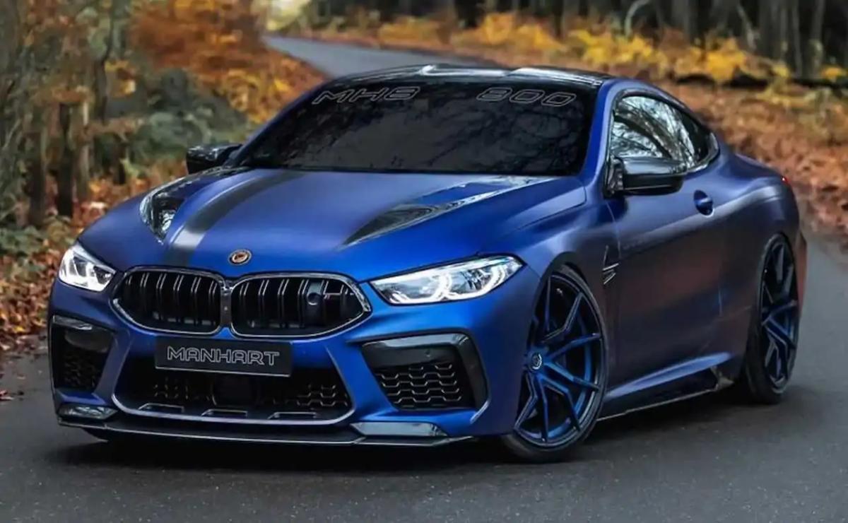 Sleek blue BMW M8 sports car on a road surrounded by autumn foliage.