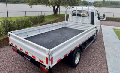 White flatbed truck parked on a gravel surface near a lake.