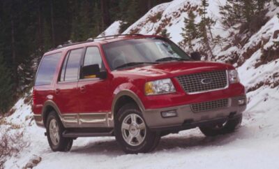 Red SUV driving through snowy terrain near a forest.