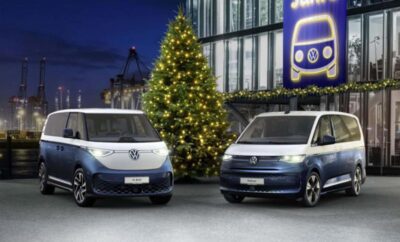 Two Volkswagen vans parked beside a decorated Christmas tree at night.
