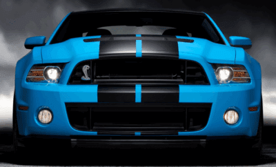 Front view of a blue sports car with black racing stripes and aggressive headlights.