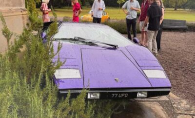 A purple Lamborghini Countach partially submerged in water with people around.