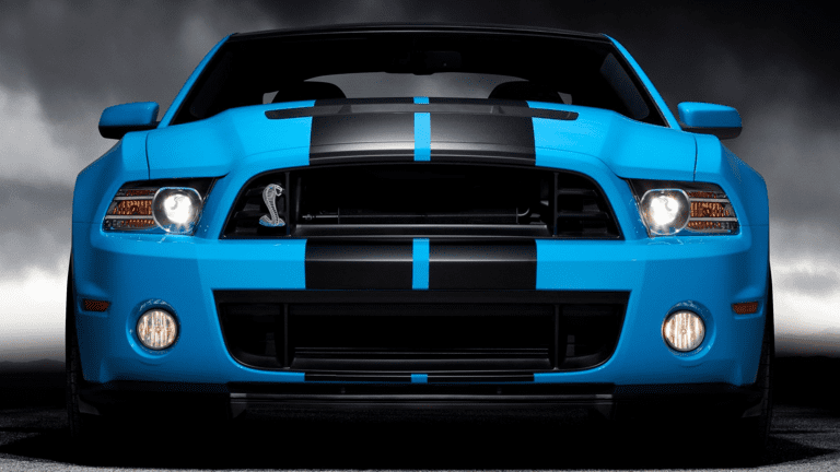 Front view of a blue sports car with black racing stripes and aggressive headlights.