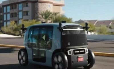 A compact autonomous vehicle parked outdoors near buildings.