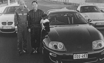 Two men posing beside a black sports car in a vintage photo.