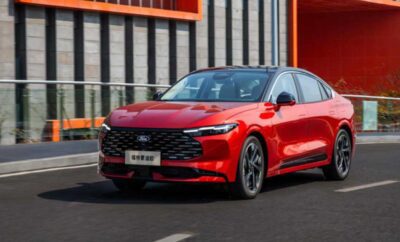 A sleek red car driving on an urban street with modern buildings in the background.