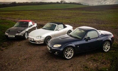 Three sporty convertible cars parked on a dirt path near open fields.