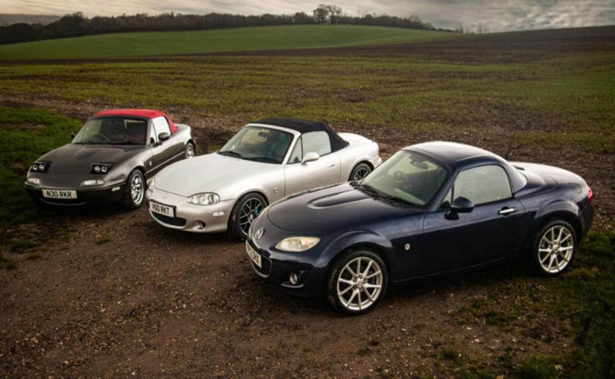 Three sporty convertible cars parked on a dirt path near open fields.