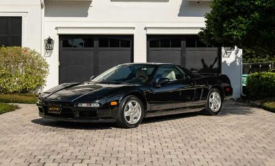 A black classic sports car parked on a brick driveway in front of a garage.