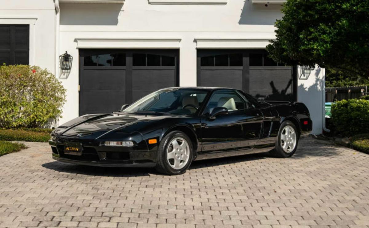 A black classic sports car parked on a brick driveway in front of a garage.
