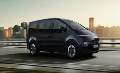 A sleek black modern van driving on a city street at sunset.