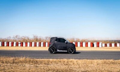 A compact black car driving on a racetrack under a clear blue sky.