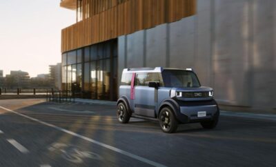 Compact electric delivery vehicle parked by a modern building at sunset.