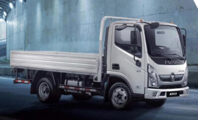 A white flatbed truck parked indoors against a blue wall.