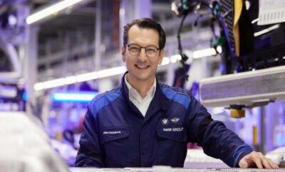 Man in a blue lab coat smiling in a high-tech lab.