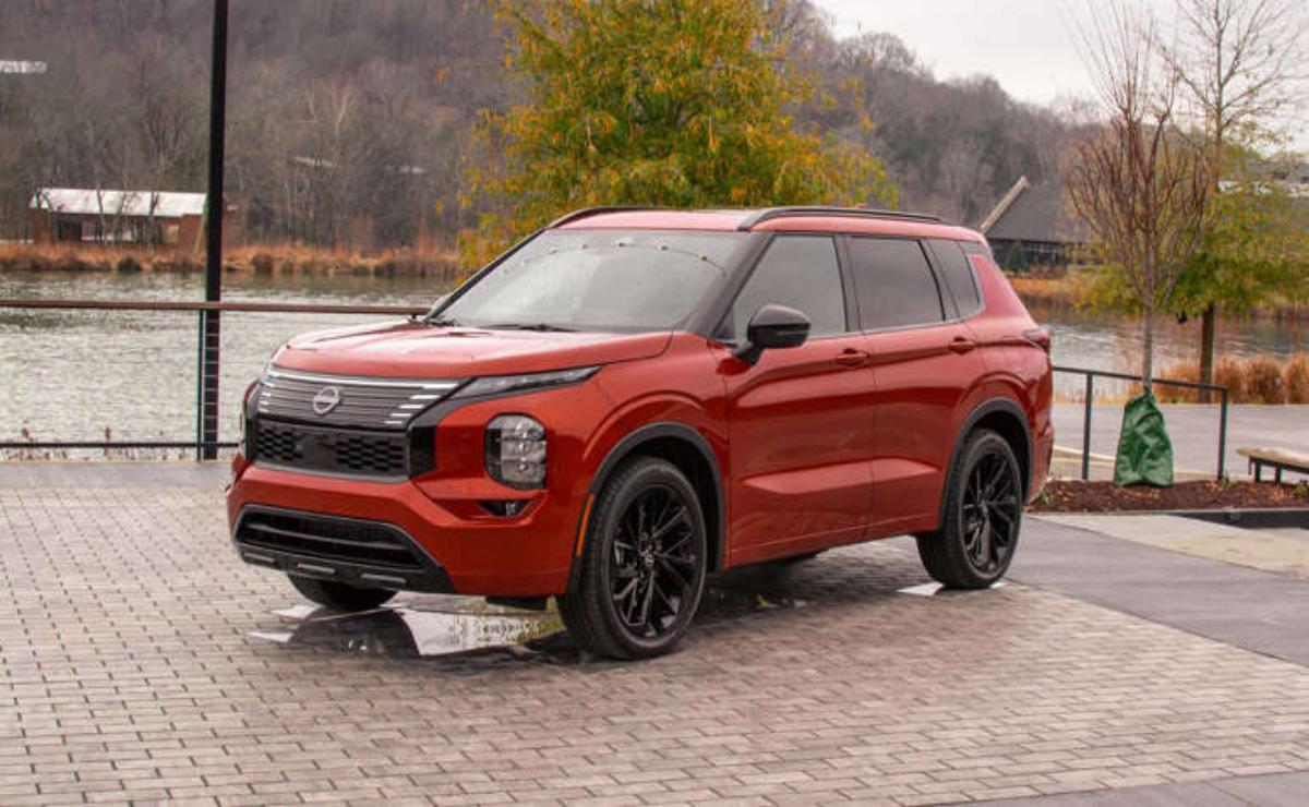 Red SUV parked on a paved area with autumn trees in the background.