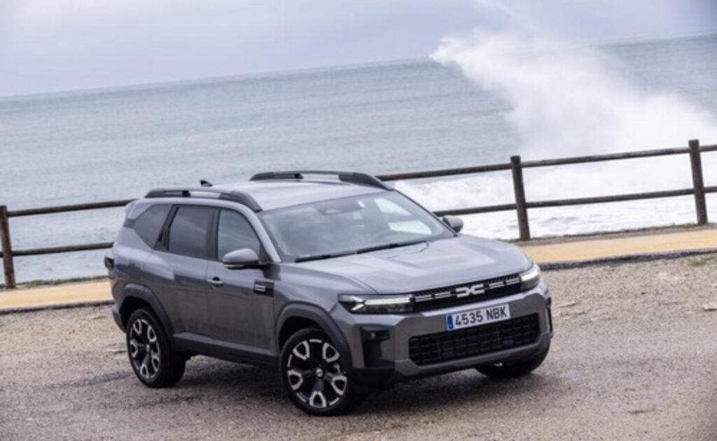 A man working on his laptop and writing in a notebook at a desk.