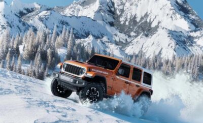Orange off-road vehicle driving through snowy mountain terrain.