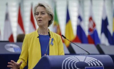 A woman speaking at a podium with various national flags in the background.