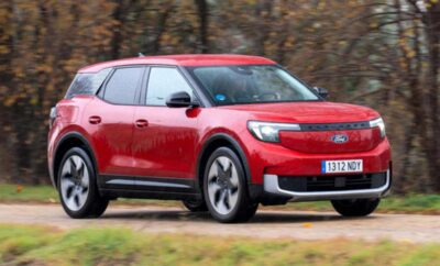 A red Kia electric SUV driving on a road with autumn trees in the background.