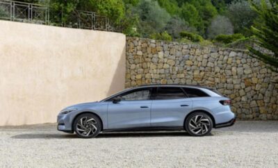Sleek silver station wagon parked by stone wall and greenery.