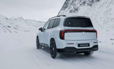White SUV driving on snowy mountain road under cloudy sky.