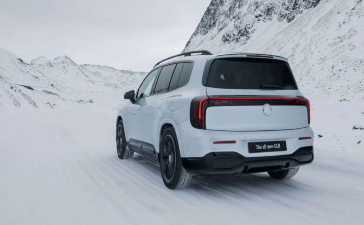 White SUV driving on snowy mountain road under cloudy sky.