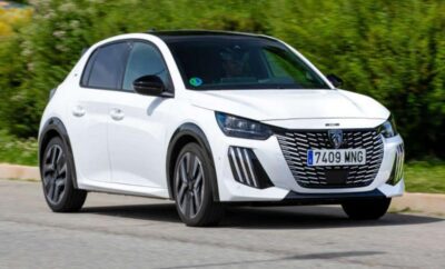 White modern compact car driving on a road surrounded by greenery.