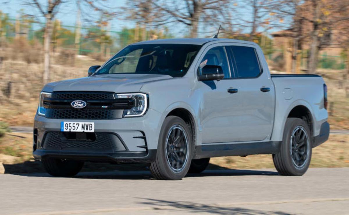 A gray electric pickup truck driving on a road with trees in the background.