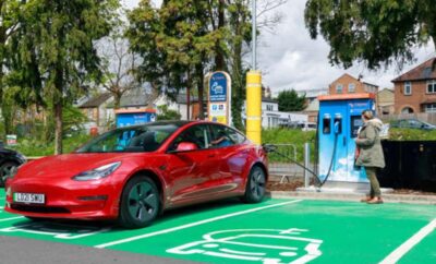 Red electric car charging at a fast-charging station in a green parking spot.