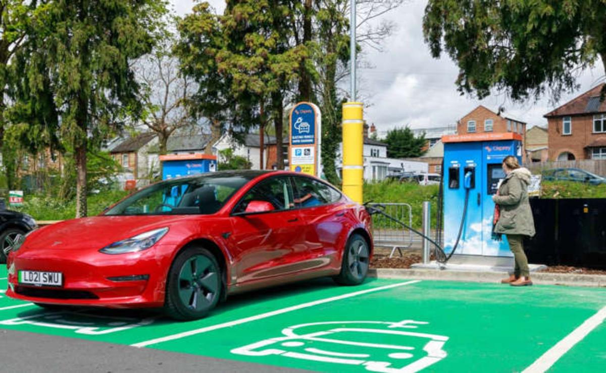 Red electric car charging at a fast-charging station in a green parking spot.